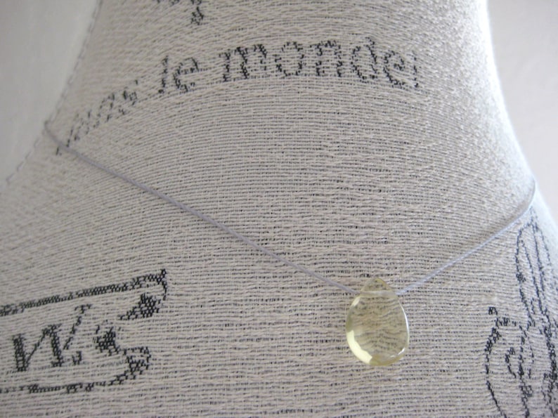 Puede incluir: Un collar sencillo con un colgante transparente en forma de l&aacute;grima. El colgante est&aacute; hecho de un material amarillo claro.