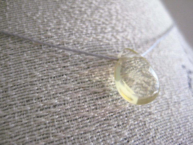 Puede incluir: Un collar delicado con un colgante de piedra preciosa amarilla facetada transparente.