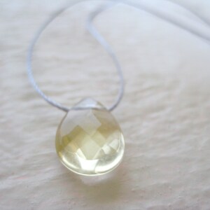 Puede incluir: Un collar delicado con un colgante de l&aacute;grima transparente facetado. El colgante est&aacute; hecho de una piedra preciosa de color amarillo claro y cuelga de un cord&oacute;n blanco fino.