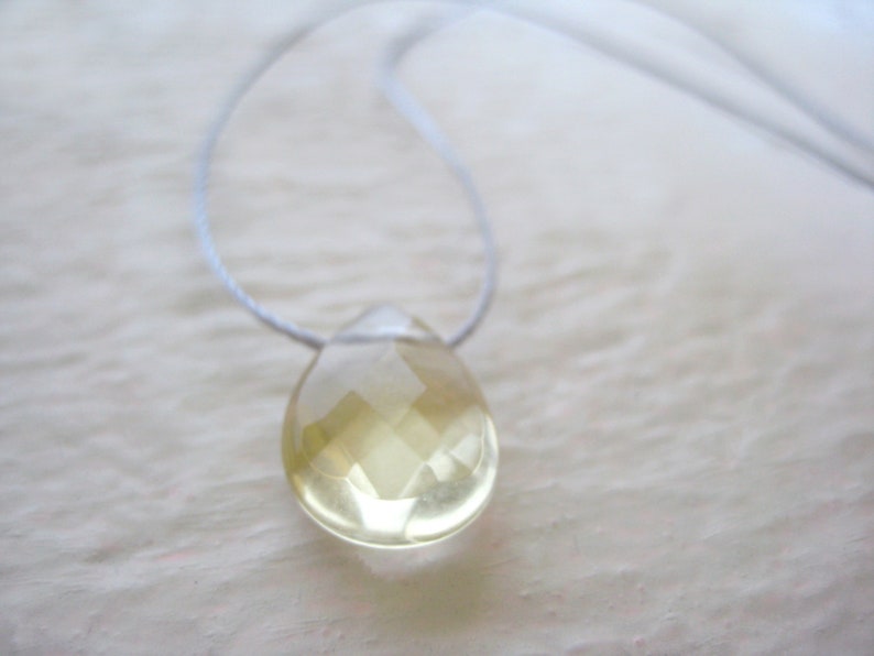 Puede incluir: Un collar delicado con un colgante de l&aacute;grima transparente facetado. El colgante est&aacute; hecho de una piedra preciosa de color amarillo claro y cuelga de un cord&oacute;n blanco fino.