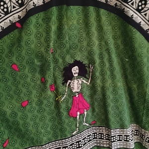 May include: Green fabric with a white and black pattern. A skeleton figure in a pink dress is holding a rose and standing on a green background.