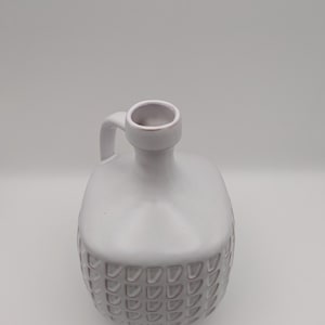 Puede incluir: Jarrón de cerámica blanco con un patrón texturizado de pequeños círculos en relieve. El jarrón tiene un cuerpo redondeado y una sola asa.