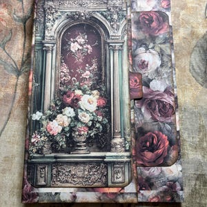 May include: A decorative journal with a floral design. The cover features a detailed illustration of a floral arrangement in a classical architectural setting, with a side panel adorned with rose imagery.