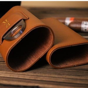 K&ouml;nnte beinhalten: Ein braunes Leder-Zigarrenetui mit integriertem Cutter. Das Etui tr&auml;gt eine goldene Inschrift "V.I.P."