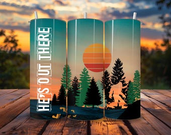 Può includere: Tre bicchieri in acciaio inossidabile con una scena di tramonto e foresta. Il bicchiere a sinistra ha la scritta "He's Out There" stampata su di esso. Il bicchiere al centro ha un grande sole arancione con un gradiente rosso, arancione e giallo. Il bicchiere a destra ha una silhouette di Bigfoot che cammina nella foresta.