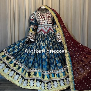 Puede incluir: Un vestido azul verdoso y dorado bordado con un chal marrón. El vestido tiene un corpiño ajustado con cuello alto y mangas largas. La falda es amplia y fluida. El chal está drapeado sobre los hombros y tiene un ribete de flecos.