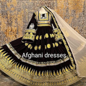 Op de afbeelding: Een zwarte en gouden geborduurde jurk met een lange rok en een bijpassende hoofddoek. De jurk heeft een ronde halslijn en lange mouwen. De rok is versierd met een gouden rand en een patroon van gouden cirkels. De hoofddoek is wit en doorschijnend.