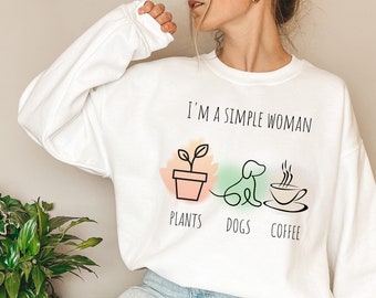 May include: White sweatshirt with the text "I'M A SIMPLE WOMAN" above illustrations of a potted plant, a dog, and a coffee cup. Below the illustrations are the words "PLANTS", "DOGS", and "COFFEE".