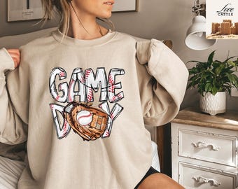 May include: A beige sweatshirt with a graphic print of a baseball glove and ball with the text "GAME DAY" in white letters.