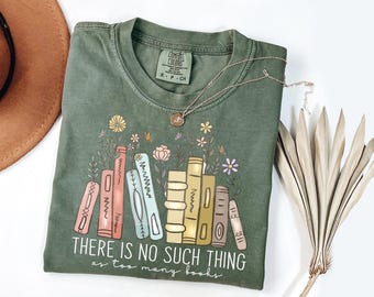 May include: Green Comfort Colors t-shirt with a graphic of colorful books and flowers. The text "THERE IS NO SUCH THING as too many books" is printed below the books. A gold necklace and dried flowers are also in the image.