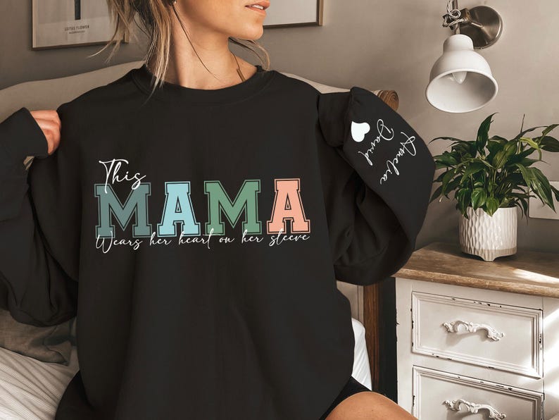 May include: Black sweatshirt with the text "This Mama wears her heart on her sleeve" in white. The word "Mama" is in colorful block letters. The sleeve has the text "Always love you" in white with a small heart.