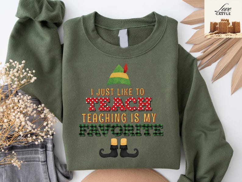 May include: Olive green sweatshirt with the text "I JUST LIKE TO TEACH TEACHING IS MY FAVORITE". The word "TEACH" is in red with white polka dots. The word "FAVORITE" is in green and black plaid. An elf hat and shoes are also featured.