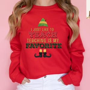 May include: A red sweatshirt with the text "I JUST LIKE TO TEACH TEACHING IS MY FAVORITE" in a festive design. The design includes an elf hat, polka dots, and plaid patterns, with elf shoes at the bottom. A fun, teacher-themed apparel item.