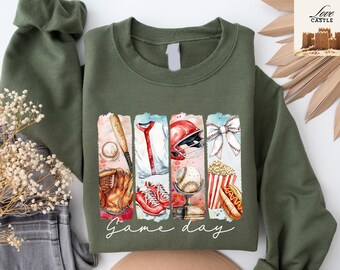 May include: Green sweatshirt with a graphic print of baseball equipment, a hot dog, popcorn, and a bow. The text "Game day" is printed below the graphic.