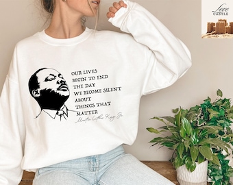 Może przedstawiać: Biała bluza z czarno-białym obrazkiem Martina Luthera Kinga Jr. i cytatem: "Nasze życie zaczyna się kończyć w dniu, w którym milczymy o rzeczach, które mają znaczenie."