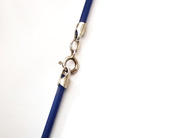 May include: A close-up of a blue necklace with a silver clasp. The necklace has a dark blue cord and a silver clasp with a ring closure. The clasp is connected to the blue cord with silver connectors.
