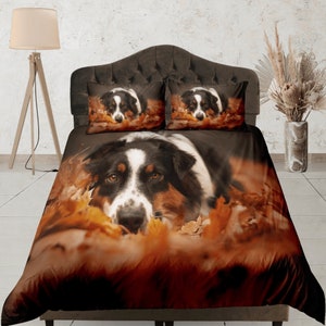 Pode incluir: Conjunto de roupa de cama com um design de cão. A capa de edredão e duas fronhas mostram um cão com pelo preto, branco e castanho, rodeado por folhas de outono. O esquema de cores é quente, com tons de castanho e laranja.