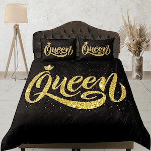 Op de afbeelding: Zwarte queensize dekbedovertrek met gouden glitterletters die "Queen" zeggen op het dekbedovertrek en op de twee kussenslopen.