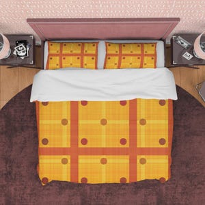 Op de afbeelding: Een gele en oranje dekbedovertrek met een geometrisch patroon van vierkanten en cirkels. Het dekbedovertrek ligt op een bed met twee bijpassende kussenslopen.