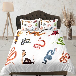 Puede incluir: Bedding blanco con un patrón de serpiente colorido. La ropa de cama presenta una variedad de serpientes en diferentes colores y poses, incluyendo una serpiente verde, una serpiente roja, una serpiente azul y una serpiente amarilla.