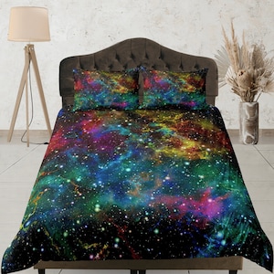 Può includere: Un letto con una testiera nera e un copripiumino e federe con stampa galassia colorata. Il copripiumino presenta uno sfondo blu scuro con nebulose e stelle verdi, gialle, rosa e viola brillanti.