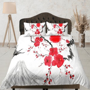 Può includere: Copripiumino bianco con un design floreale rosso e nero. Il design presenta un ramo di ciliegio stilizzato con fiori rossi e accenti di inchiostro nero. Il copripiumino presenta anche una montagna stilizzata e un sole rosso.