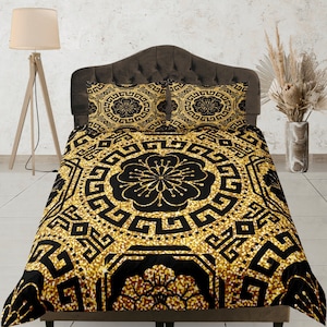 Op de afbeelding: Zwart en gouden beddengoedset met een geometrisch patroon. De dekbedovertrek en kussenslopen hebben een herhalend ontwerp van in elkaar grijpende vierkanten en cirkels.
