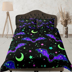 Puede incluir: Una funda nórdica negra con un patrón repetido de murciélagos y estrellas en verde neón, rosa y morado. La funda nórdica está en una cama con dos fundas de almohada a juego.