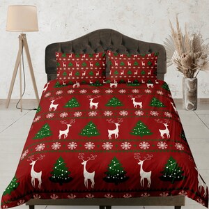 May include: Red Christmas bedding set with a white reindeer and green Christmas tree pattern. The set includes a duvet cover and two pillowcases.