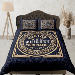 May include: A black and gold duvet cover with a large, circular design featuring the text "BOSTON WHISKEY YOUR NAME DISTILLER'S". The design is surrounded by a decorative border of leaves and swirls. Two matching pillowcases with a smaller version of the design are also included.