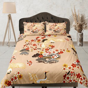 Puede incluir: Funda nórdica beige con un patrón floral y de grúas. El patrón presenta grúas rojas, amarillas y grises volando sobre una rama de flores blancas y rosas.