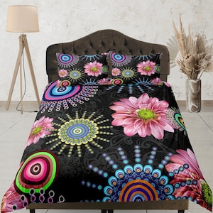 May include: A black bedspread and two pillowcases feature a vibrant floral design. Large pink flowers and colorful circular patterns are set against a dark background. The bedding set adds a pop of color to any bedroom.