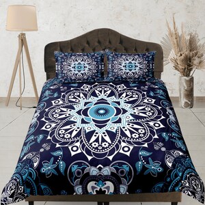May include: A navy blue duvet cover with a large white and blue mandala design. The duvet cover features a floral pattern with butterflies and leaves. The duvet cover is on a bed with two matching pillowcases.