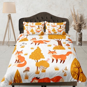 Op de afbeelding: Wit beddengoed met een herhalend patroon van oranje vossen, gele bomen en bruine paddenstoelen. Het beddengoed is gemaakt van zachte, comfortabele stof en is perfect om elke slaapkamer een vleugje whimsy te geven.