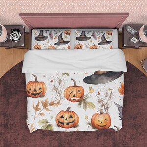 May include: White bedding with a Halloween theme featuring a pattern of orange pumpkins with jack-o-lantern faces and black witch hats on a white background with brown leaves and vines.