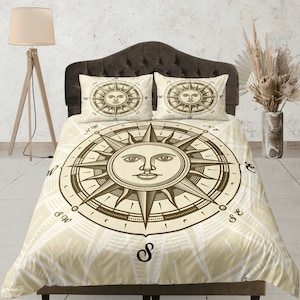 May include: A beige duvet cover with a brown compass design featuring a sun with a face. The compass points are labeled with the letters N, S, E, and W. The duvet cover has a subtle pattern of white lines.