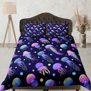 Op de afbeelding: Een donkerblauwe dekbedovertrek met een kleurrijk kwallenpatroon. Het dekbedovertrek heeft verschillende kwallen in verschillende kleuren en maten, waaronder roze, paars, blauw en groen. De kwallen zijn willekeurig op het dekbedovertrek geplaatst, wat een grillig en speels ontwerp creëert.