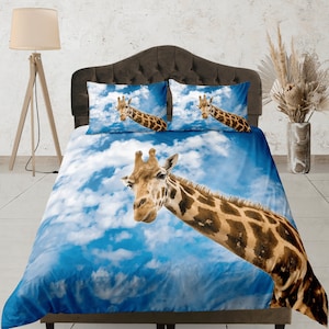 Könnte beinhalten: Ein blauer und weißer Bettbezug mit einem Giraffenmuster. Der Kopf der Giraffe schaut aus dem oberen Teil des Bettbezugs heraus, und ihr Hals ist über den Bettbezug gestreckt. Die Giraffe ist braun und weiß mit einem gefleckten Muster. Der Bettbezug ist aus weichem, bequemem Stoff.