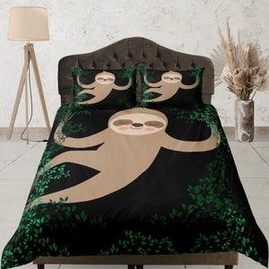 Può includere: Un copripiumino nero e verde con un bradipo dei cartoni animati appeso a un ramo. Il bradipo è marrone con la pancia bianca e ha un'espressione felice. Il copripiumino ha un motivo a foglie verdi.