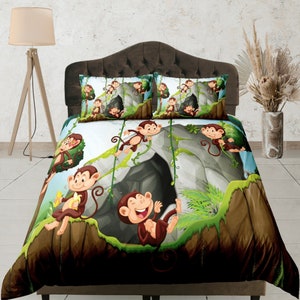 May include: A white and brown duvet cover with a cartoon illustration of monkeys playing in a cave. The duvet cover features a green, brown, and gray color scheme and includes a cave with vines and a monkey hanging from a vine.