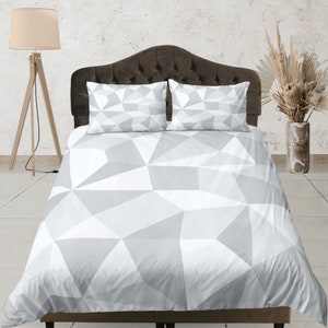 May include: A white and gray geometric patterned duvet cover with two matching pillowcases. The duvet cover has a modern, abstract design.