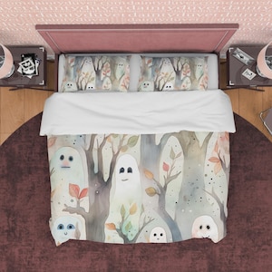 May include: A white duvet cover with a watercolor design of ghosts in a forest. The ghosts are white with black eyes and smiles. The forest is a light green and brown with leaves in shades of orange, red, and yellow. The duvet cover is on a bed with two matching pillowcases.