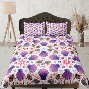 May include: A white duvet cover with a purple and pink seashell pattern. The duvet cover is on a bed with two matching pillowcases.