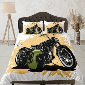 Pode incluir: Um conjunto de roupa de cama branco e amarelo com uma ilustração em preto e branco de uma motocicleta. A motocicleta tem um capacete verde com uma estrela branca.