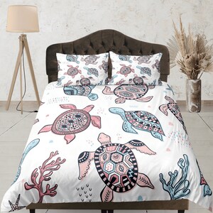 Könnte beinhalten: Weiße Bettwäsche mit einem farbenfrohen Muster mit Meeresschildkröten und Korallen. Die Bettwäsche hat ein rosa, blaues und schwarzes Farbschema.