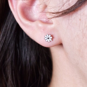 May include: A close-up of a person's ear with a small white flower stud earring.