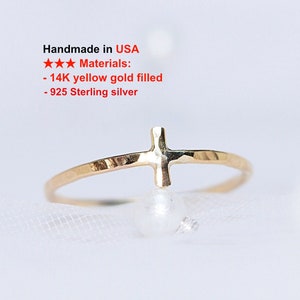 May include: A delicate gold-filled ring featuring a cross design. The ring is made of 14K yellow gold filled and 925 sterling silver. The ring is shown on a white surface. The text "Handmade in USA" is visible in the image.