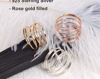 May include: Three handmade rings in yellow gold, rose gold, and sterling silver. The rings are spiral-shaped and sit on a white surface with a black accent. The text "Handmade in USA" is visible.
