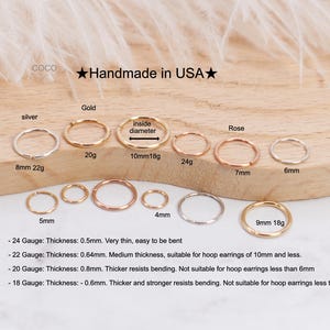 May include: A collection of small hoop earrings in silver, gold, and rose gold tones, displayed on a wooden surface. The earrings vary in size and gauge, with text indicating measurements in millimeters and gauge sizes. The text "Handmade in USA" is also visible.