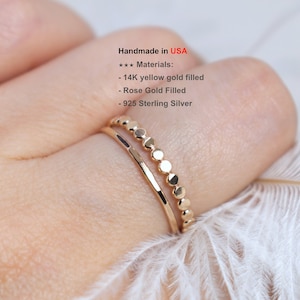 May include: Two gold rings on a finger. The top ring is a delicate band with small round beads. The bottom ring is a simple, thin band. Handmade in USA. Materials: 14K yellow gold filled, Rose Gold Filled, 925 Sterling Silver.